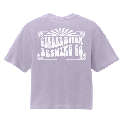 A light lavender purple short-sleeve t-shirt shown from the back, featuring a large white distressed graphic that reads 'CELEBRATION BREWING CO' with a sunburst design above it.