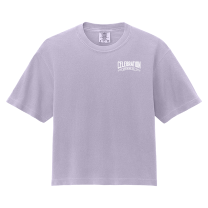 A light lavender crewneck t-shirt with a white graphic print on the left chest reading 'CELEBRATION' and 'ONE CELEBRATING EVERY DAY'. The shirt is displayed flat against a solid white background.