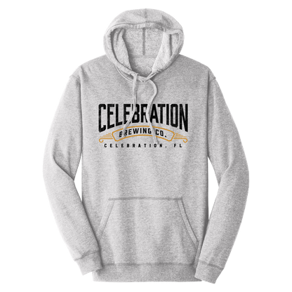 A light heather gray pullover hoodie with a front kangaroo pocket and drawstring hood, featuring a black and gold graphic print on the chest that reads 'CELEBRATION BREWING CO. CELEBRATION, FL'.